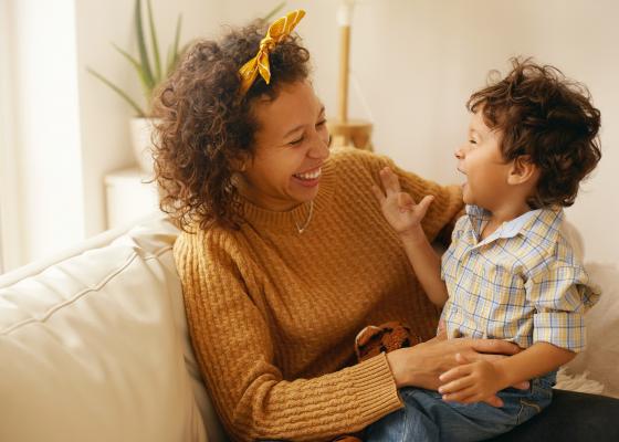 Mother and toddler son laughing on sofa.